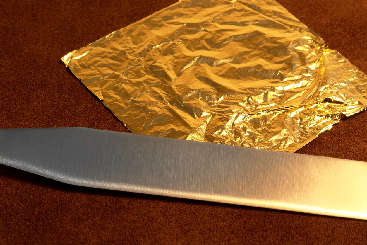 gilding theme with a leaf of beaten gold and blade on brown leather surface in warm ambiance